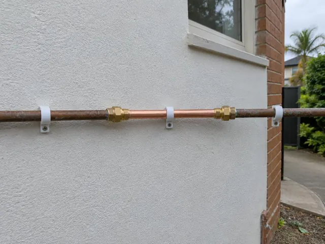 Repaired copper water pipe on an exterior wall beside a brick corner in Narrabeen