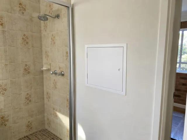 Bathroom shower wall with a neat white access panel beside tiled shower area in Newport