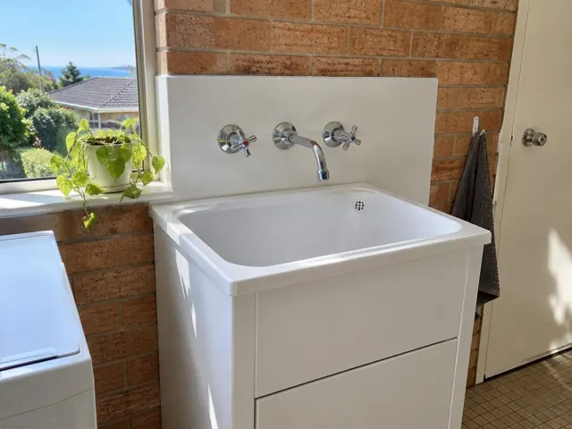 White laundry sink with chrome taps and spout against a brick wall in Dee Why